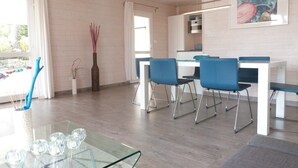 A modern kitchen with white cabinets, a dining area with blue chairs, and a glass coffee table.