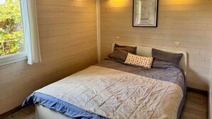 A bedroom with a bed, a framed picture, an air conditioning unit, and a window with curtains.
