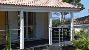 A covered outdoor area with a metal railing, steps leading to a door marked with the number 79, and a view of a hill and trees in the background.