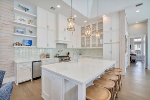 A spacious kitchen with white cabinetry, a large island with stools, and pendant lighting.