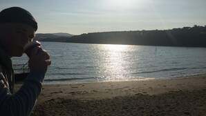 A person holding a cup by a lakeside with a clear sky and distant hills.