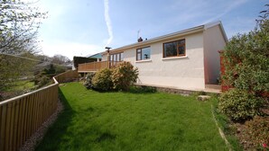 A modern two-story house with a balcony, a well-maintained lawn, and a garden with various plants.