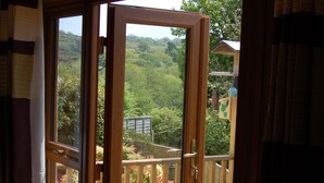 A wooden-framed glass door leading to a wooden deck with a view of greenery and a distant building.