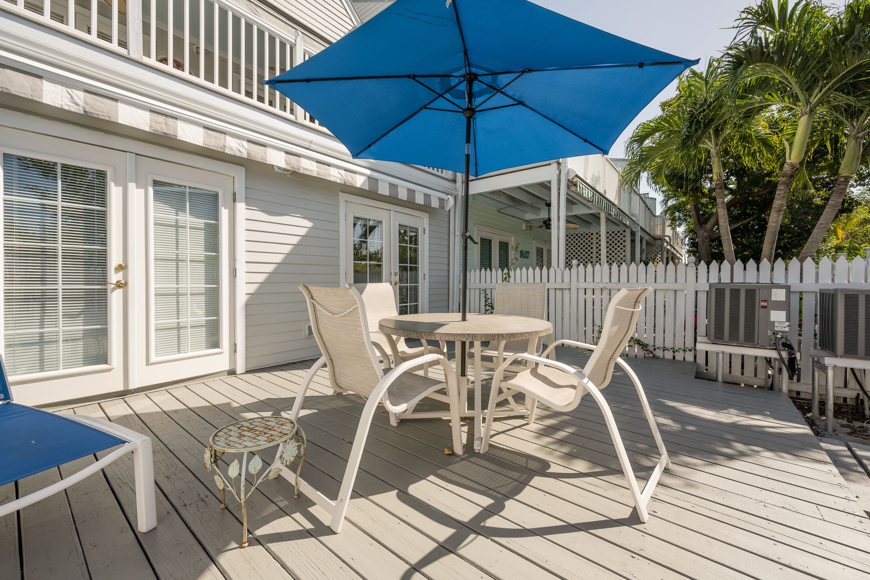 A deck with a table and chairs, a blue umbrella, and a white picket fence.