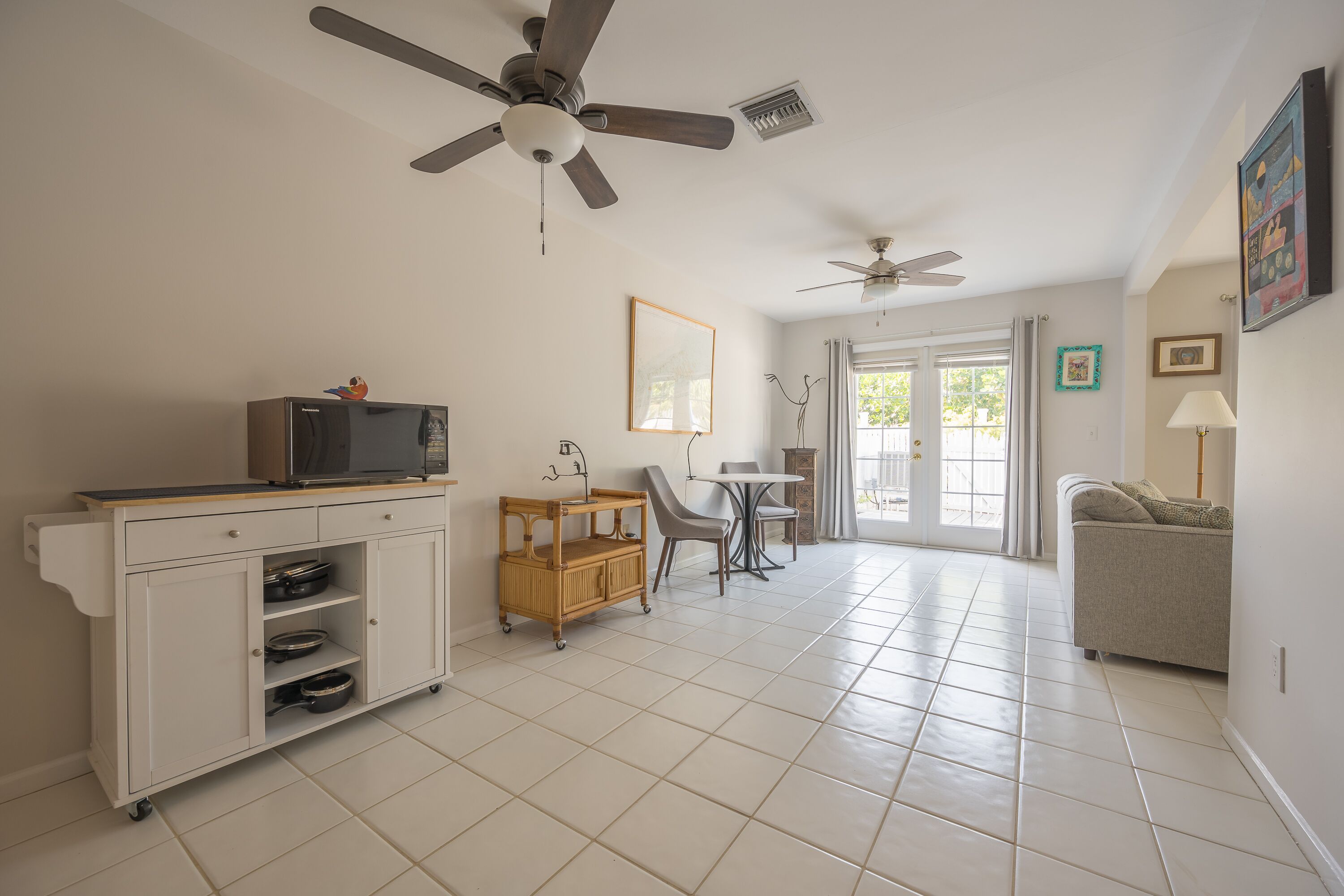 A spacious living area with a kitchen, dining table, and a sofa. There are ceiling fans, a refrigerator, and a cabinet with dishes.