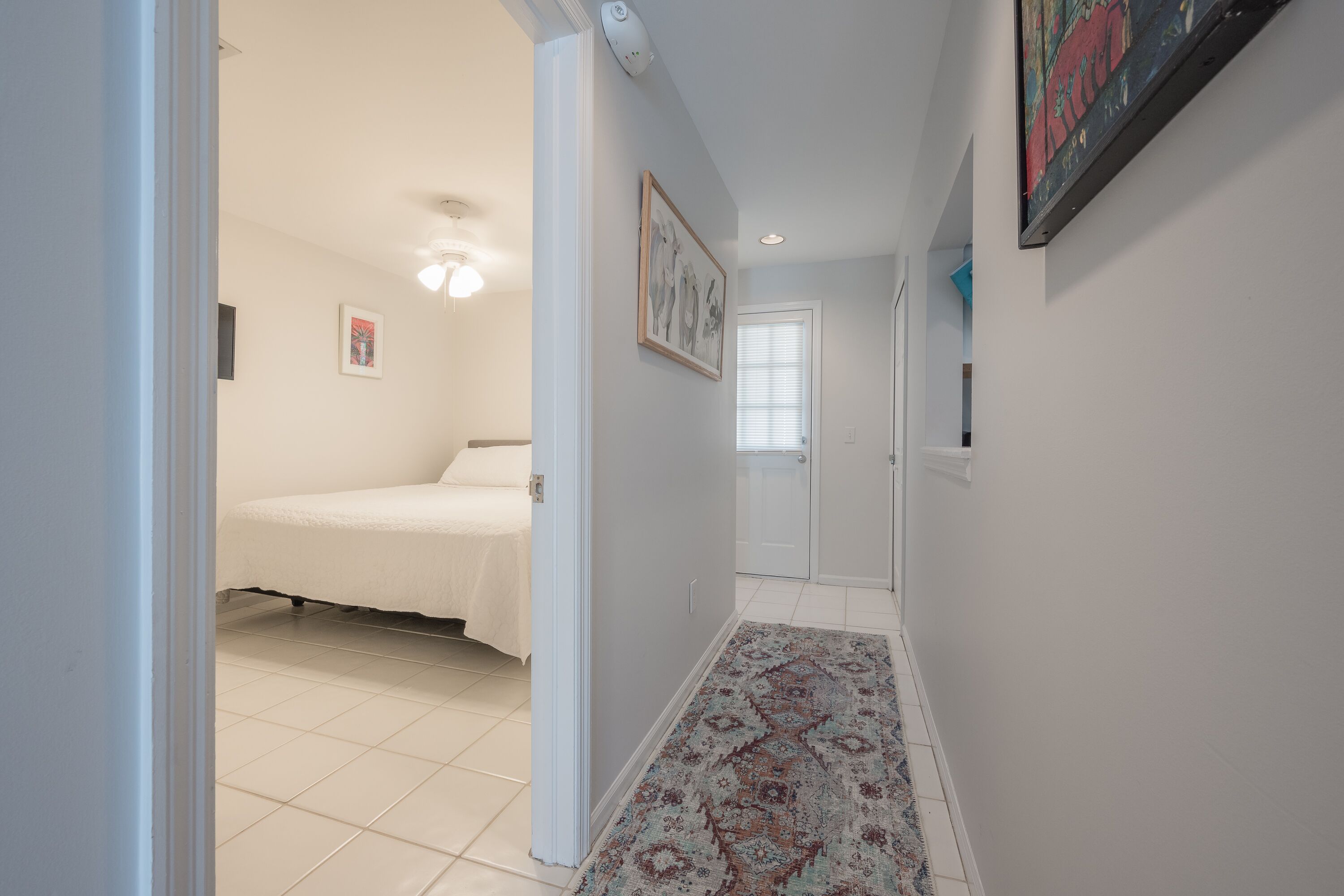 A hallway leading to a bedroom with a bed, a patterned rug, and a door with a window.