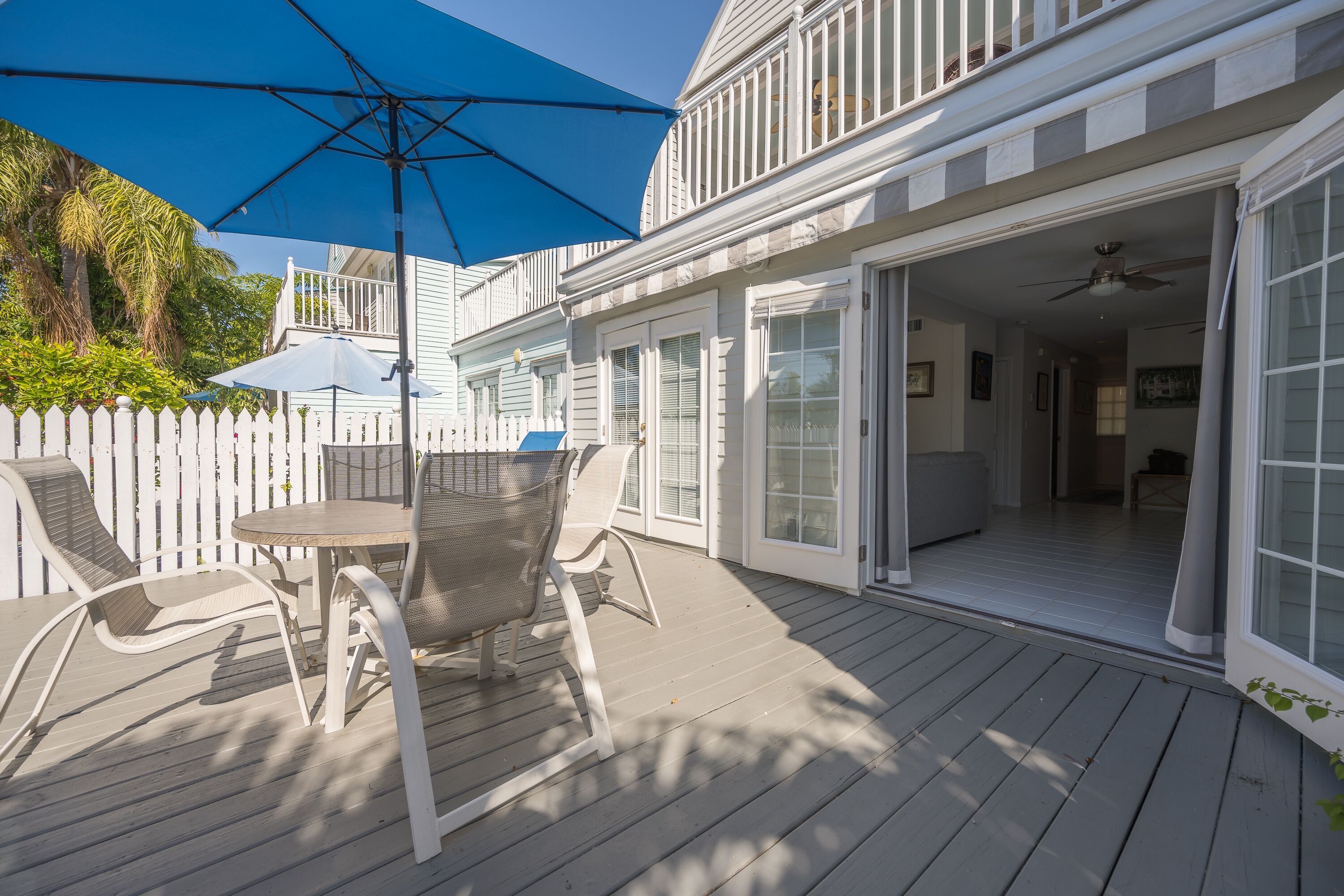 A covered patio with a table and chairs, a blue umbrella, and a white fence.