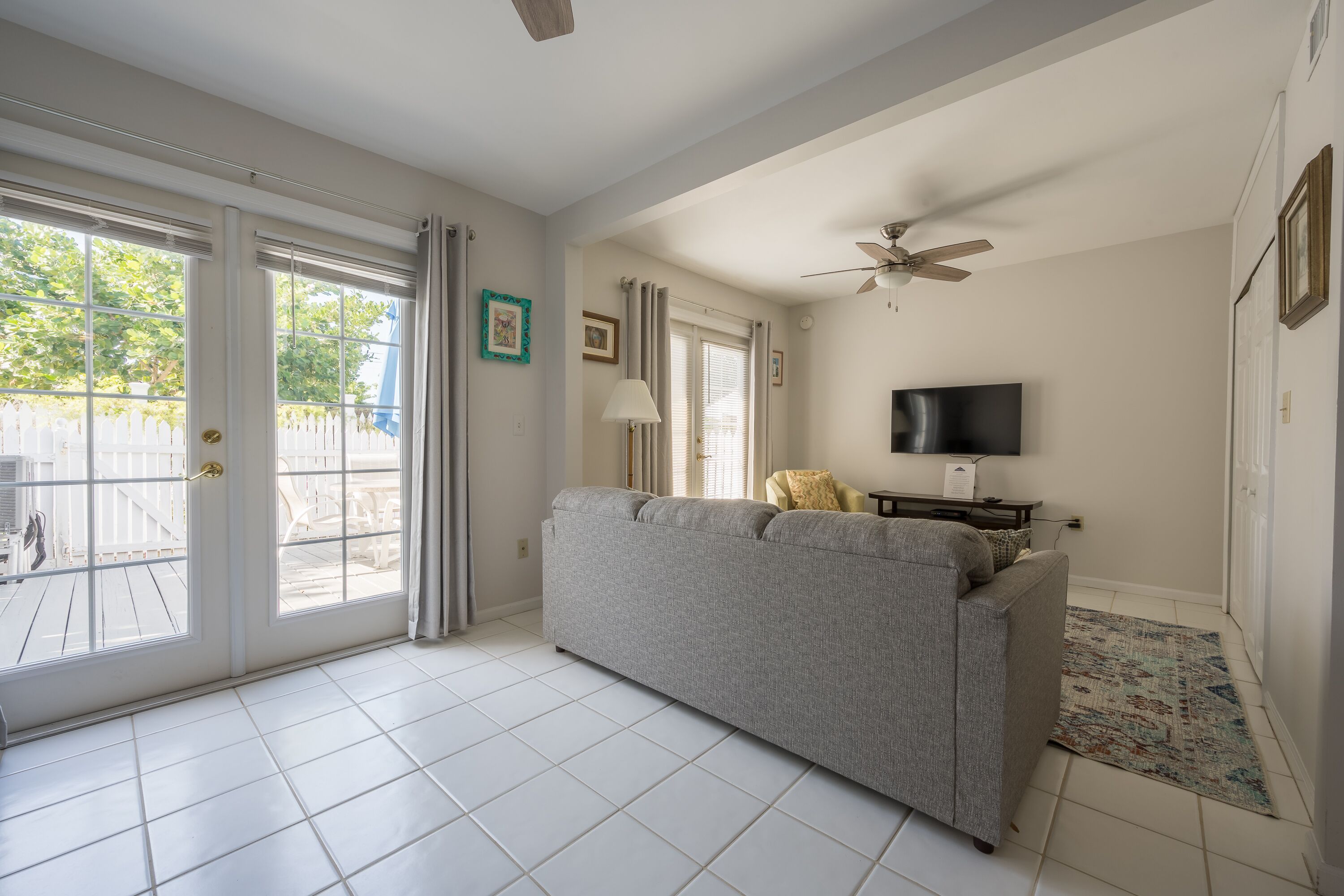 A living room with a grey sofa, a ceiling fan, a flat-screen TV, and a patterned rug.