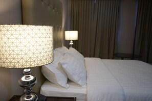 A neatly made bed with white linens, a lamp with a geometric patterned shade, and a bedside table with a remote control. - Hotel Le Duc (Dagupan)