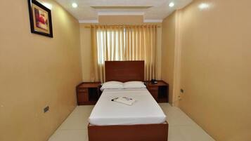 A hotel room with a single bed, a nightstand, a bedside table, and a framed picture on the wall.