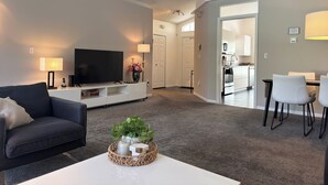 Ein modernes Wohnzimmer mit Flachbildfernseher, einer Couch, einem Couchtisch mit Dekoration und einem Essbereich mit Stühlen und Tisch.