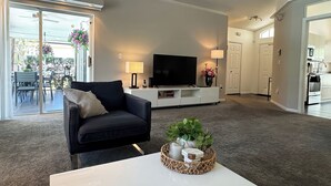 Ein modernes Wohnzimmer mit einem schwarzen Sofa, einem weißen Couchtisch, einem Flachbildfernseher und einem Essbereich mit Tisch und Stühlen.