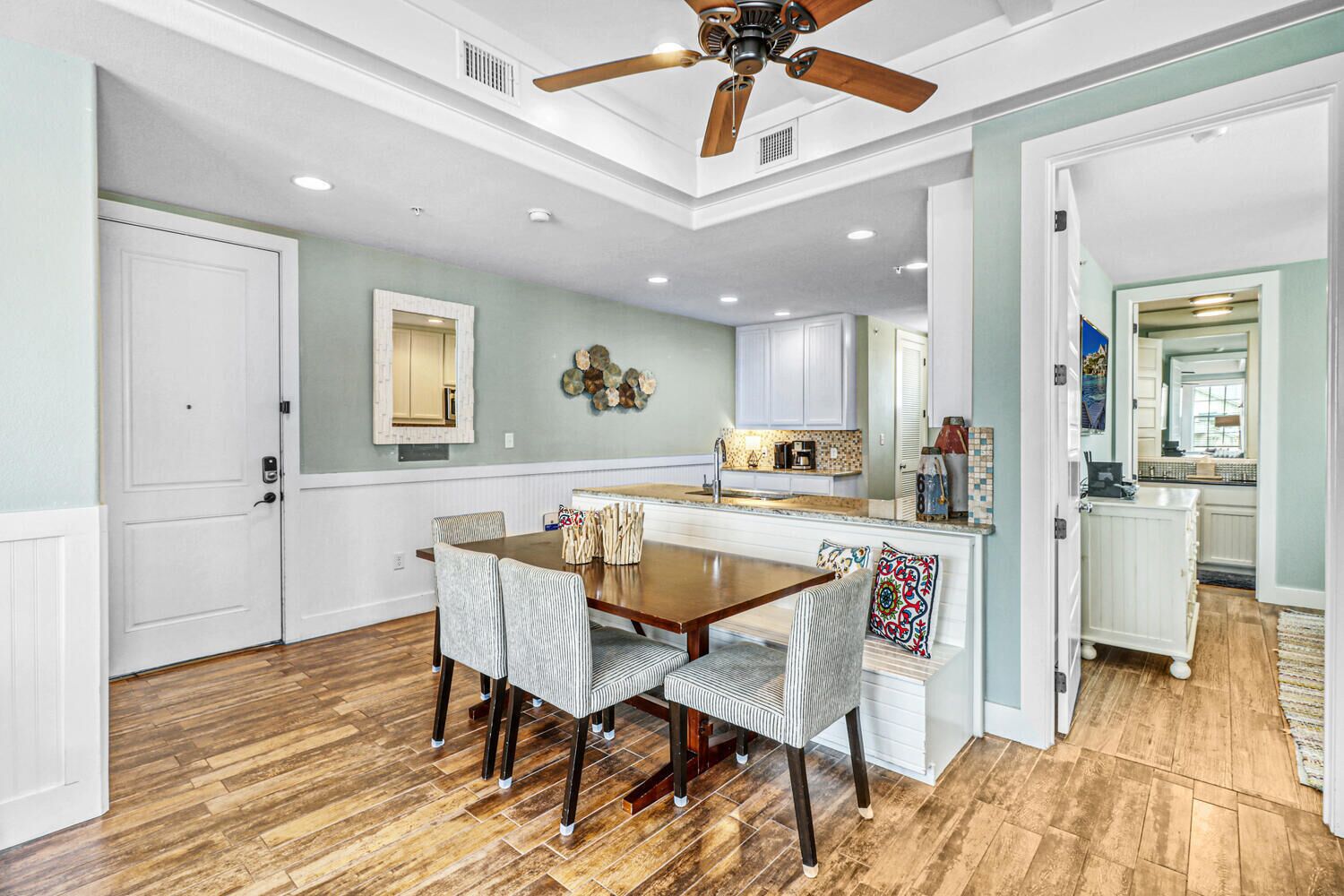 A dining area with a wooden table and chairs, a ceiling fan, and a kitchen in the background.