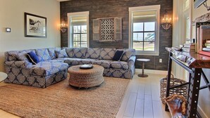 A living room with a sectional sofa, a round ottoman, and a decorative wall piece. - Escape to 'The Refuge,' an Inviting Cinnamon Shore Condo w/  Great Amenities (Port Aransas)