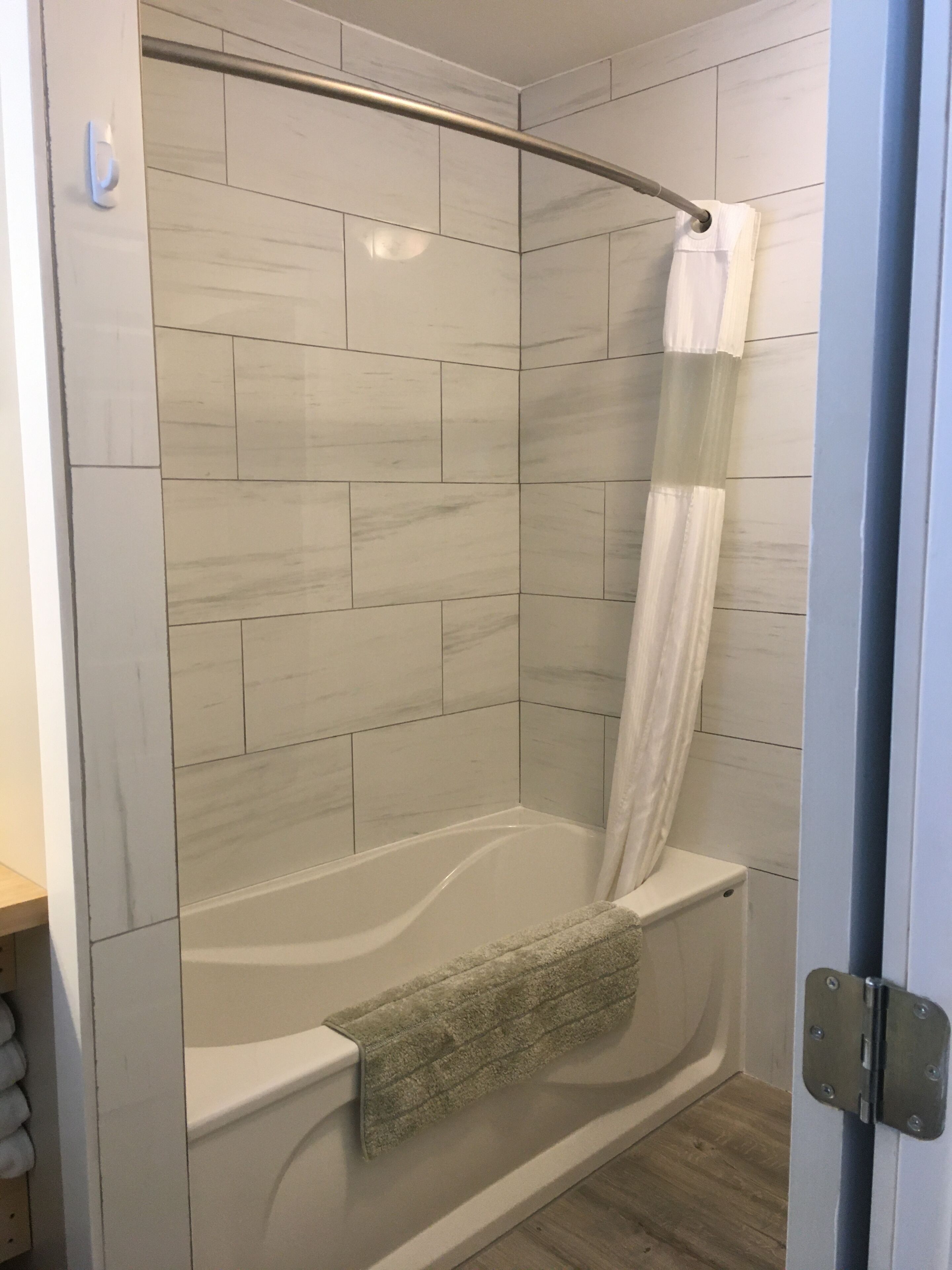 A modern shower with a curved glass door, white tiled walls, and a wooden floor.