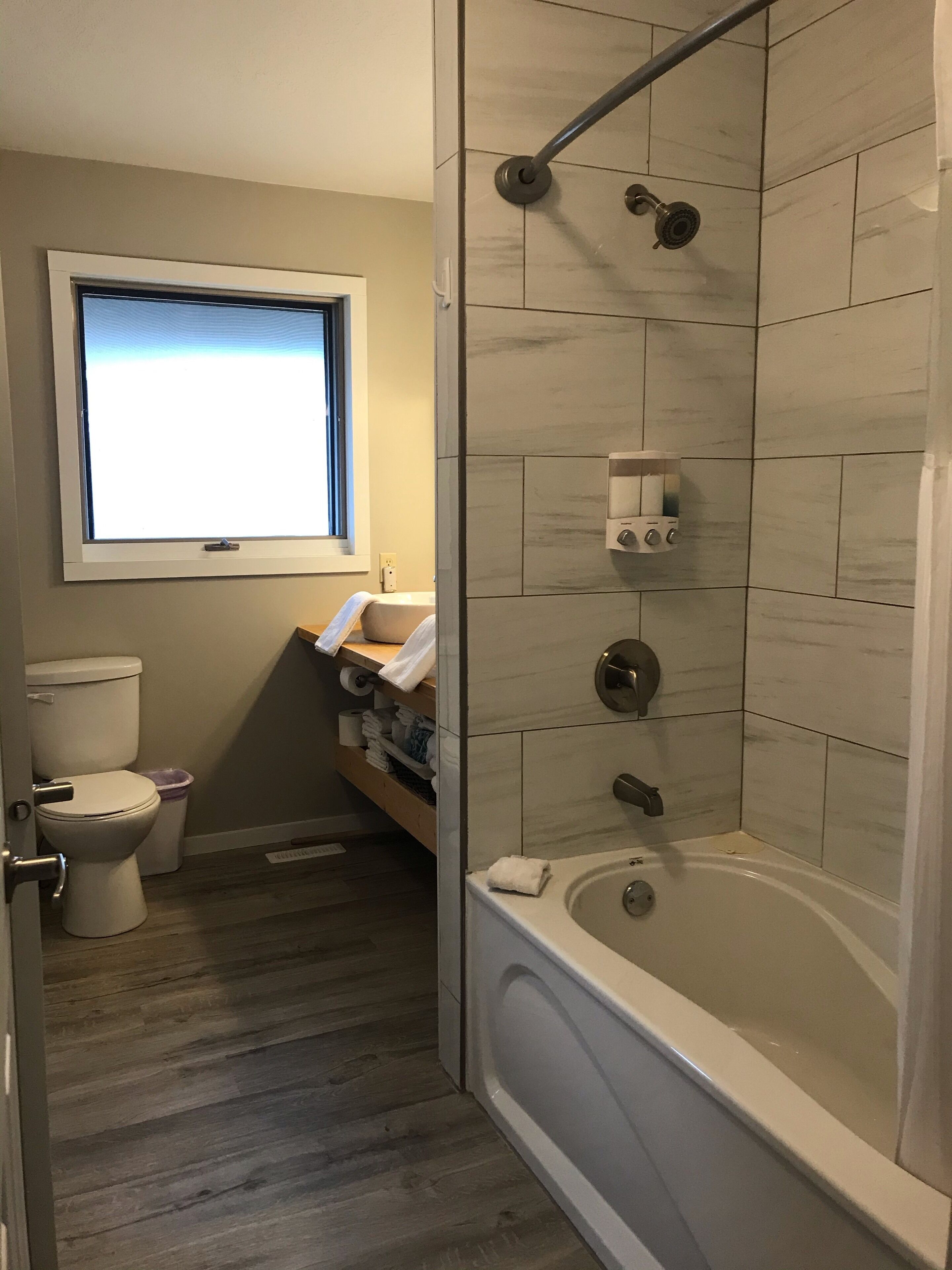 A bathroom with a toilet, a shower with a glass door, a window, and a towel rack.