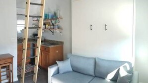 A compact living space with a built-in wardrobe, a ladder for storage, a sofa, and a small table. - Studio Condo (Newly Renovated) - 150' to Beach 20 min to Portland (Scarborough)