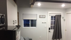 A room with a gray couch, a white door with a black curtain, a window with a view of the night sky, and a sign that reads "beachhouse". - Studio Condo (Newly Renovated) - 150' to Beach 20 min to Portland (Scarborough)