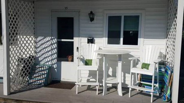 A white house with a porch, a door marked '15', and two white chairs with green cushions. - Studio Condo (Newly Renovated) - 150' to Beach 20 min to Portland (Scarborough)