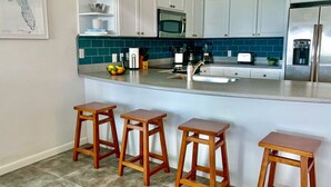 Une cuisine moderne avec des meubles blancs, un pare-feu turquoise, un réfrigérateur en acier inoxydable et un coin bar avec des tabourets.