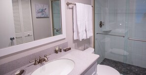 Une salle de bain avec un lavabo blanc, un miroir, une douche en verre et des toilettes.