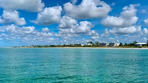 Une vue sur la côte, avec une eau turquoise cristalline, une plage de sable et une rangée de bâtiments blancs, le tout sous un ciel dégagé.
