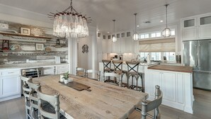 A spacious kitchen with a wooden dining table, white cabinetry, and pendant lighting.