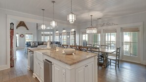 A spacious kitchen with a large island, pendant lighting, and a dining area with wooden chairs.