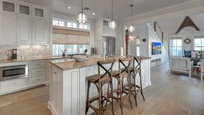 A spacious kitchen with white cabinetry, a large island with bar stools, and pendant lighting.