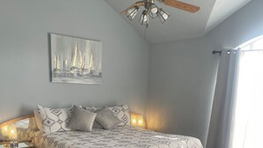 A bedroom with a bed, a ceiling fan, a nightstand, a lamp, a rug, and a window with curtains. - Spacious 4BR Retreat with Pool and Spa (Rowlett)