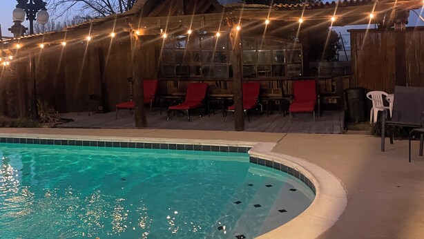 A swimming pool with a duck, a wooden building with red chairs, and string lights. - Spacious 4BR Retreat with Pool and Spa (Rowlett)