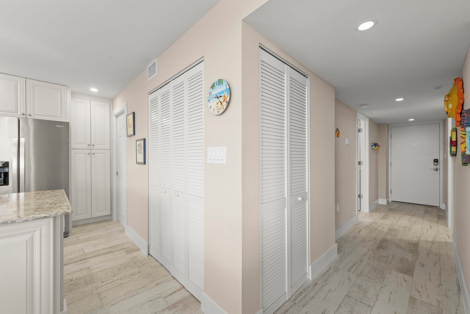 A hallway with white cabinets, a refrigerator, and a clock on the wall.