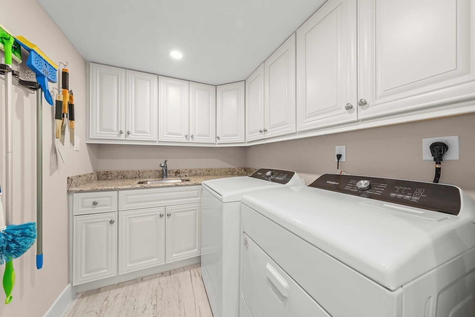 A laundry room with white cabinets, a washing machine, and a countertop with a sink.