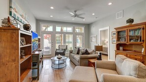 A spacious living room with a large window, a ceiling fan, and a wooden cabinet with books.