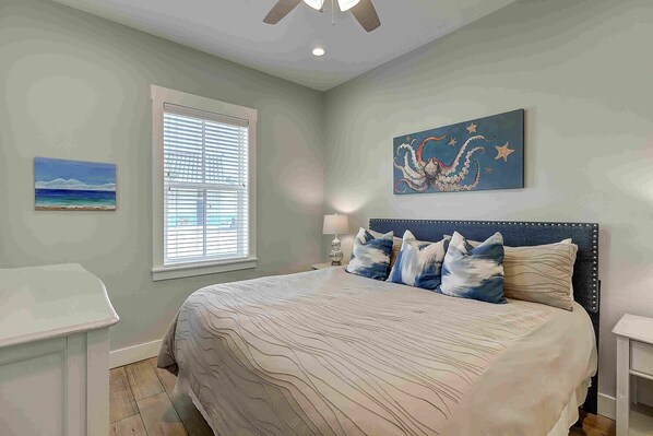 A bedroom with a bed, a nightstand, a lamp, a window with blinds, and a painting on the wall.