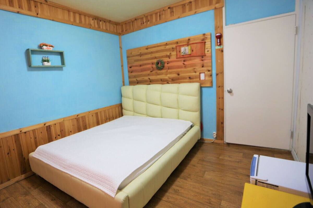 Ein Schlafzimmer mit Bett, Holzvertäfelung, einer Ablage mit Flaschen und einer Tür.
