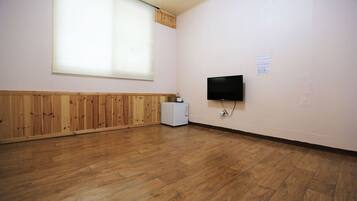 Una habitación con piso de madera, un televisor montado en la pared y una ventana con persianas.