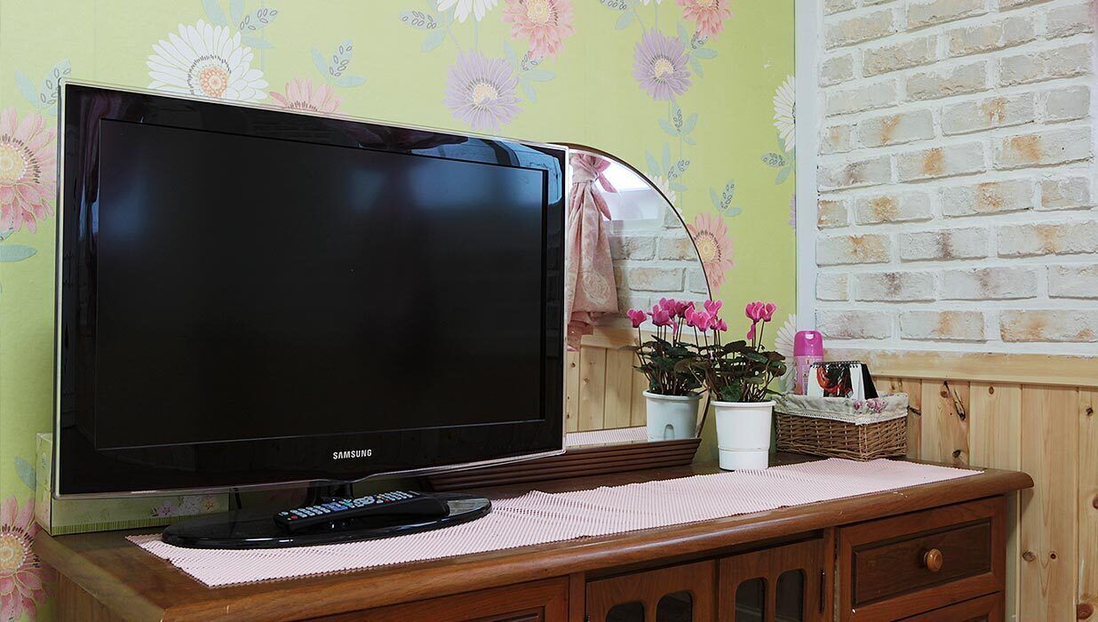 A Samsung TV on a wooden cabinet with a floral wallpaper background and a brick-patterned wall.