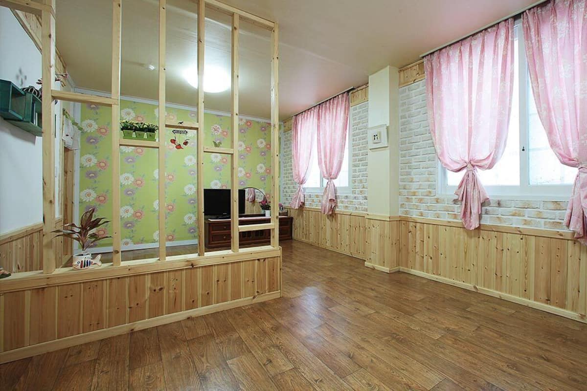 Ein Zimmer mit Holzwänden, Holzboden, einem Fernseher und rosa zurückgebundenen Vorhängen.