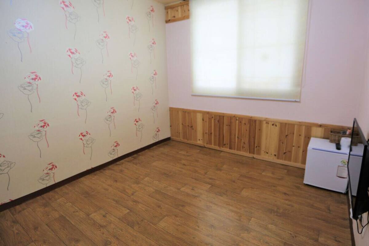 Ein Zimmer mit Holzboden, einem Heizkörper, einem Fenster mit Jalousien und einem kleinen weißen Gerät rechts.
