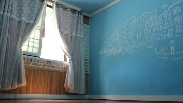 Una habitación con un ventanal grande, cortinas blancas y una pared azul con un dibujo arquitectónico en blanco.