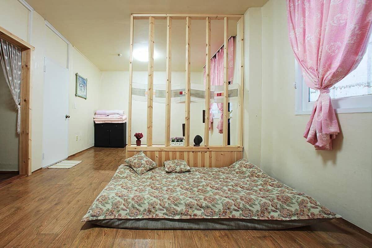 Ein Schlafzimmer mit hölzernem Bettgestell, einem floralen Bettbezug und einem Fenster mit rosa Vorhängen.