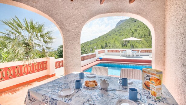 Eine Terrasse mit Pool, Esstisch und Stühlen mit Blick auf eine gebirgige Landschaft.