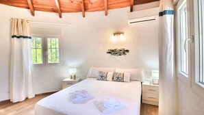 Ein Schlafzimmer mit Holzboden, einem Bett mit weißen Leinen, zwei Nachttischen mit Lampen und einem Fenster mit Vorhängen.
