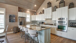 A spacious kitchen with a central island, white cabinetry, and a wooden ceiling.