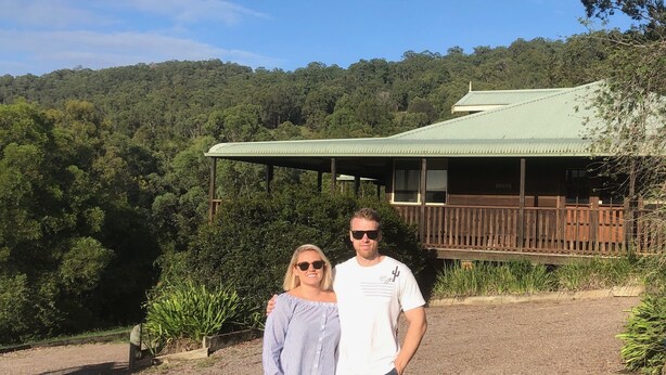 Two people standing in front of a building with a green roof and wooden deck.