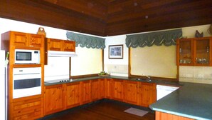 A kitchen with wooden cabinets, a microwave, an oven, a sink, and a window with a view of the outside.