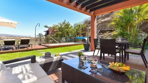 An outdoor patio with wicker furniture, a glass table, and a bowl of fruit.
