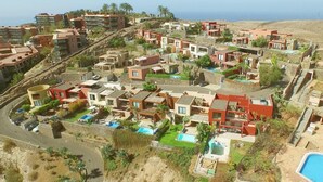 A coastal resort with modern villas, swimming pools, and a view of the sea.