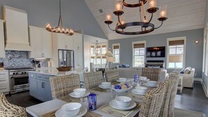 A spacious kitchen with modern appliances, a dining area with a large island, and a cozy seating area with wicker furniture. - Stunning Designer Home w/ Pool Views+Access to Cinnamon Shore Amenities (Port Aransas)